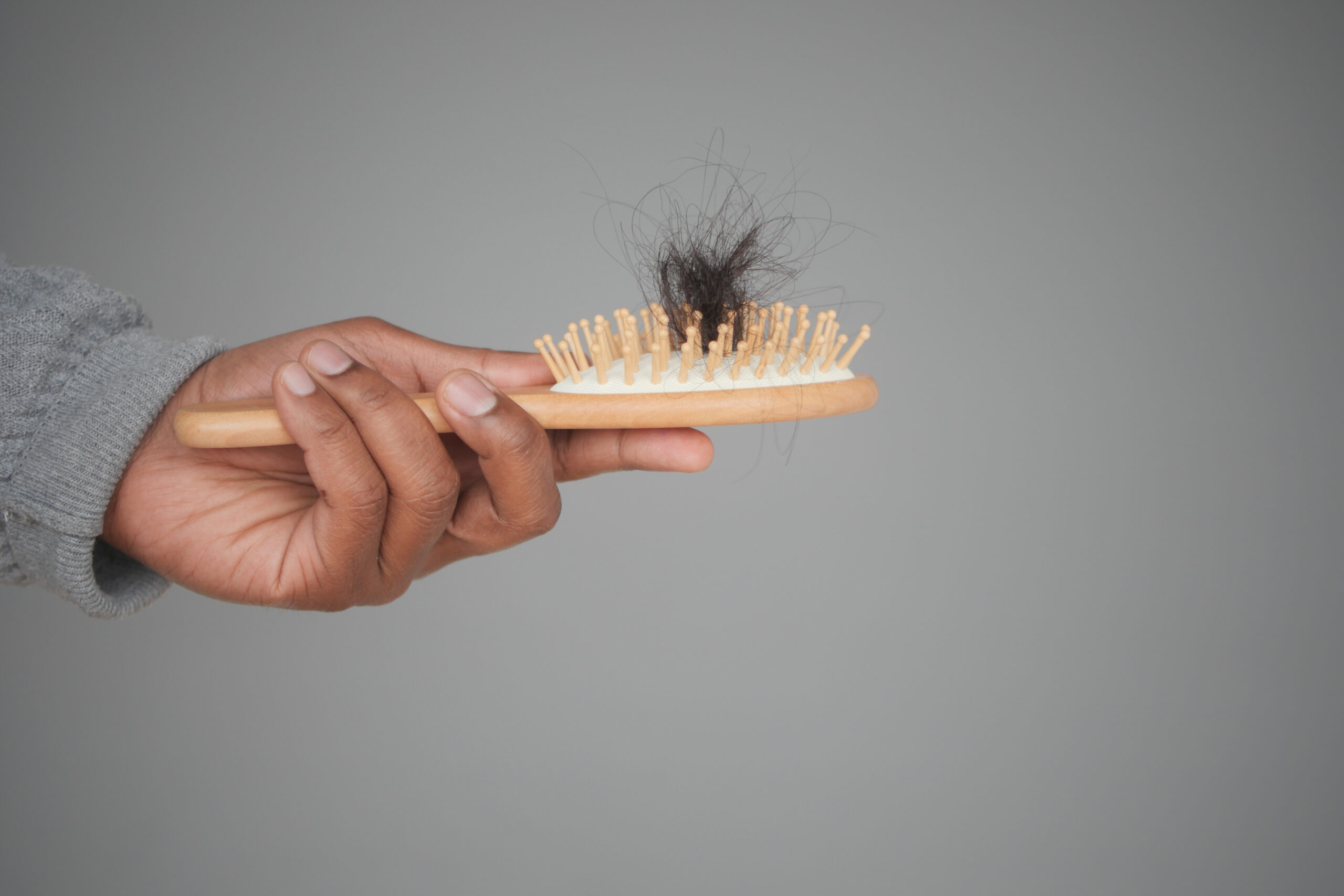 A person holding a boar bristle brush with hair stuck between the bristles, demonstrating how to clean a boar bristle brush.