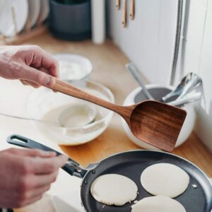 Twelve-piece set of natural teak wooden kitchen utensils including spatulas, slotted spoons, soup spoons, serving utensils, and stirring tools, designed for cooking and serving
