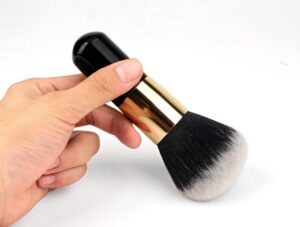 Professional vegan foundation makeup brush with dense black and white synthetic bristles, gold ferrule, and black handle for foundation, concealer, powder, and cosmetic blending.