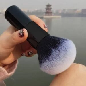 Professional vegan foundation makeup brush with dense black and white synthetic bristles, gold ferrule, and black handle for foundation, concealer, powder, and cosmetic blending.